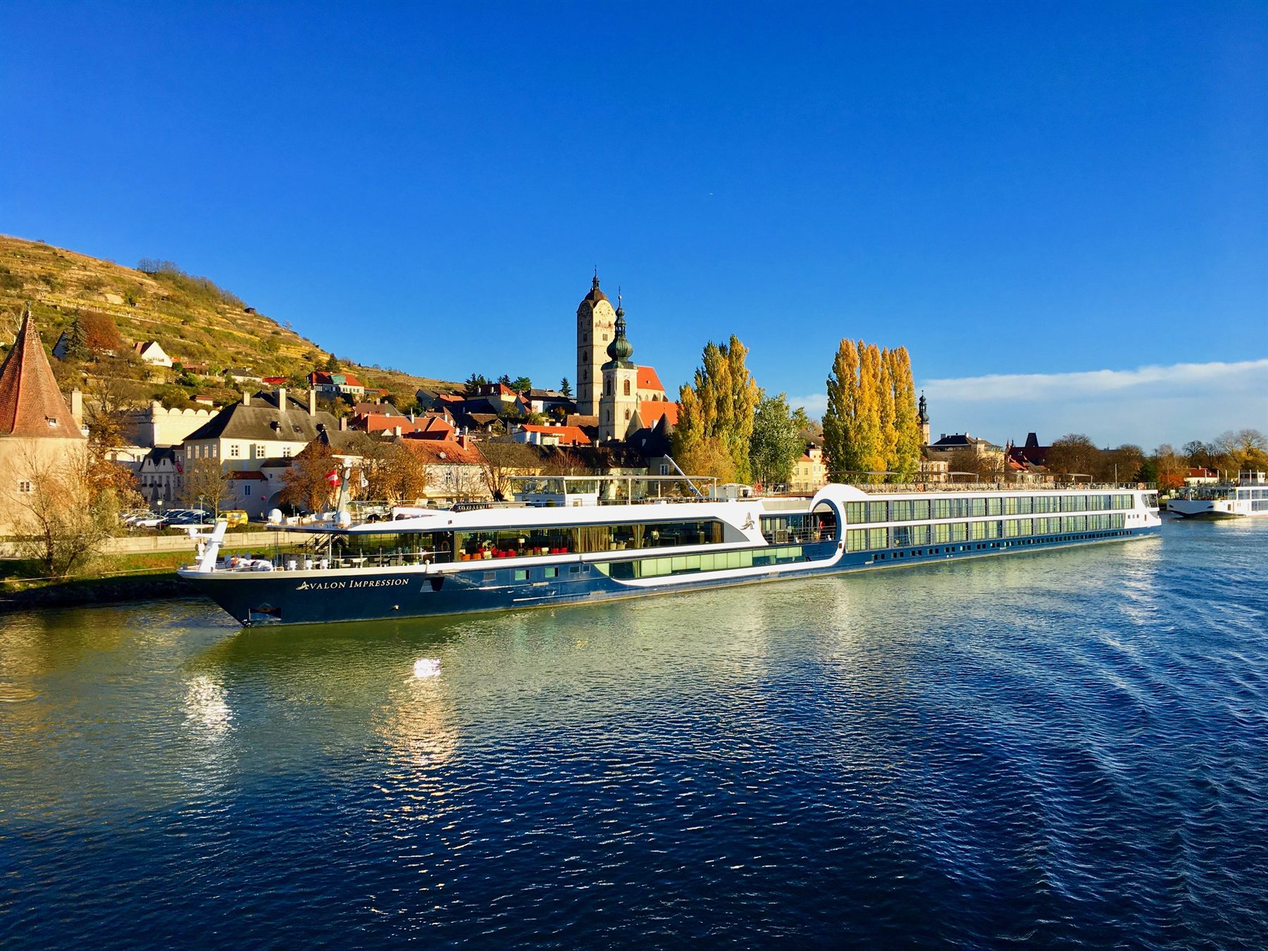 An Avalon river cruise ship docked on the Danube amid fall colors